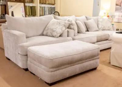 Beige sectional sofa with matching ottoman and patterned throw pillows displayed in a furniture showroom setting