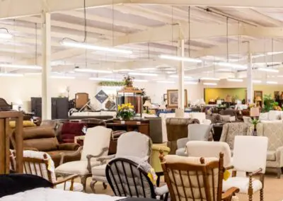 Showroom interior of Auburn Furniture with rows of sofas, upholstered chairs, recliners and mattresses displayed under bright warehouse lighting, wood and fabric finishes visible throughout